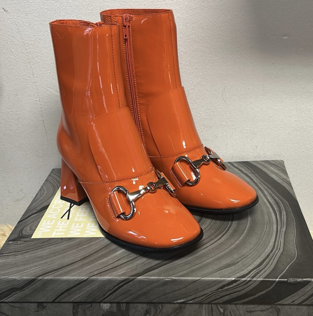 A pair of orange leather boots with a buckle across the front.