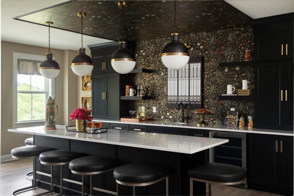 Black custom kitchen with floral wallpaper, quartz island, and globe pendant lights.