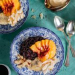 Black rice breakfast bowl with sliced peaches, coconut, and almonds in a blue patterned bowl.