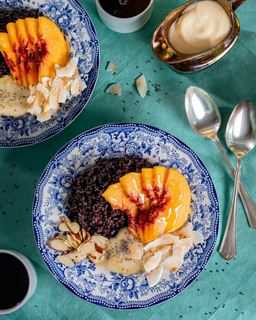 Black rice breakfast bowl with sliced peaches, coconut, and almonds in a blue patterned bowl.