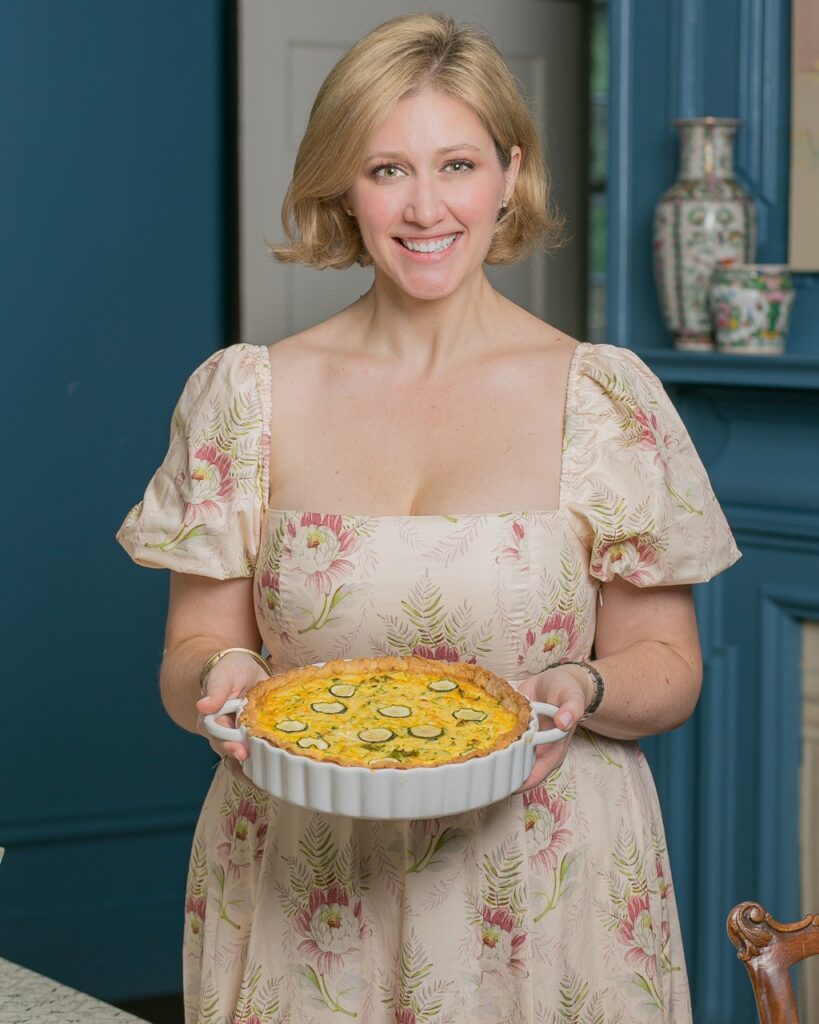 Melissa Ewen in a white dress holds her white ceramic tray of Zucchini Quiche.