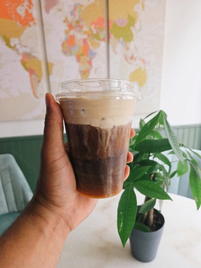 Hand holding a layered iced coffee with cream, Pittsburgh coffee.
