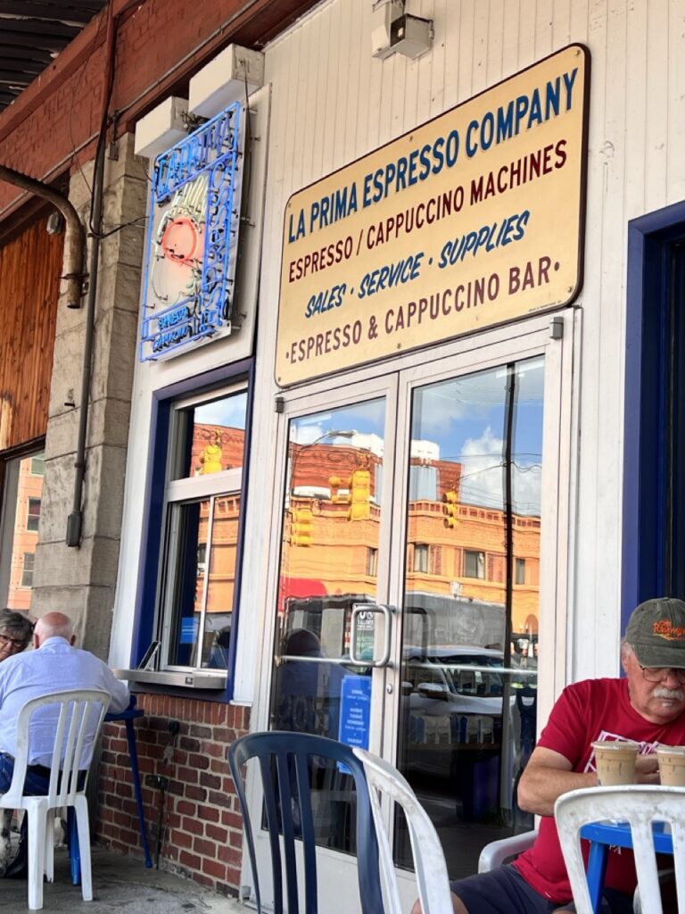 La Prima Espresso Company sign and storefront in Pittsburgh, with people seated outside.