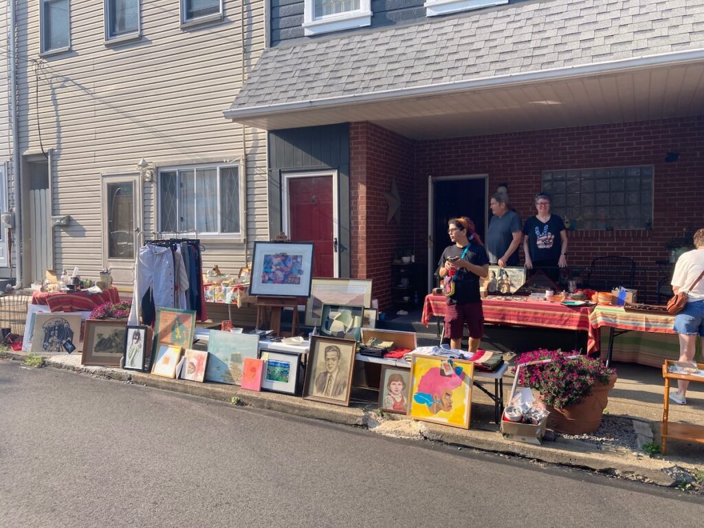 Bloomfield sidewalk sale features artwork, clothing, and household items displayed outside.