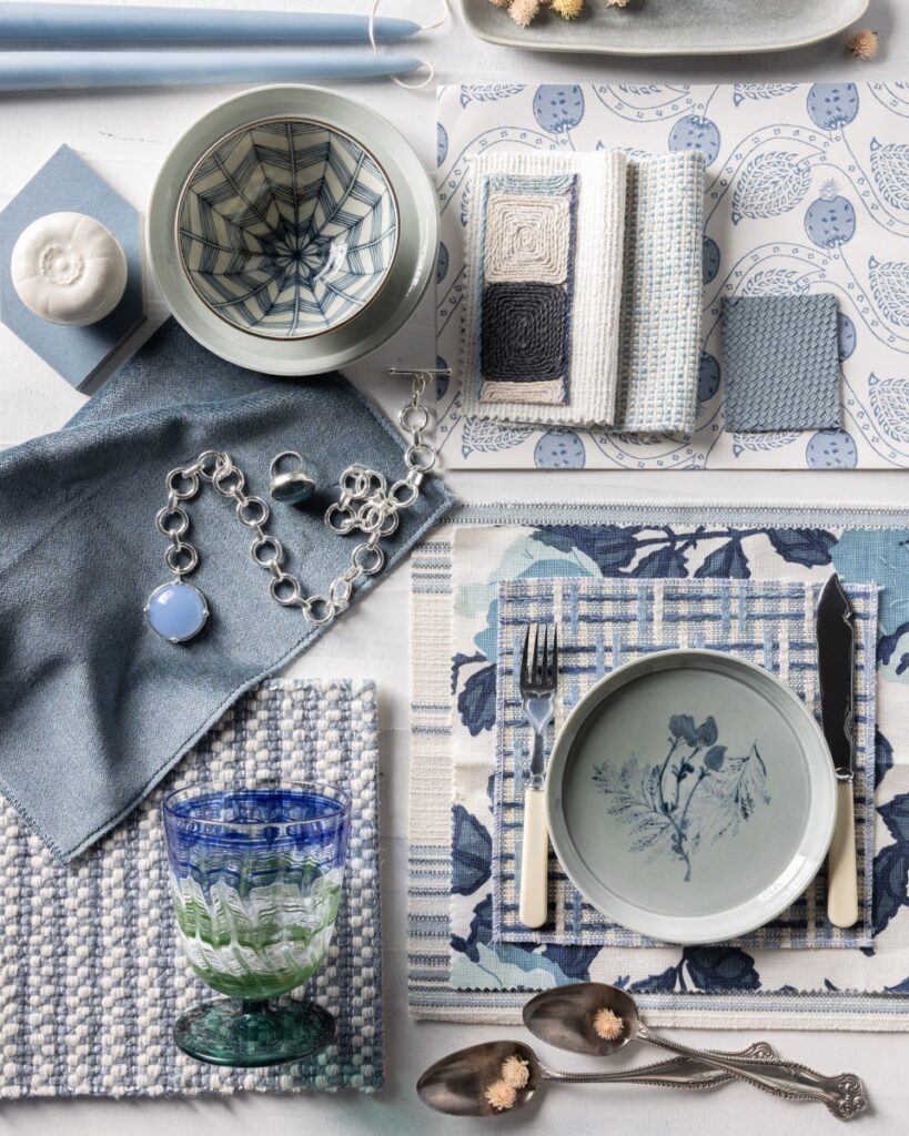 Blue and white table setting mood board with patterned ceramics, woven placemats, and glassware.