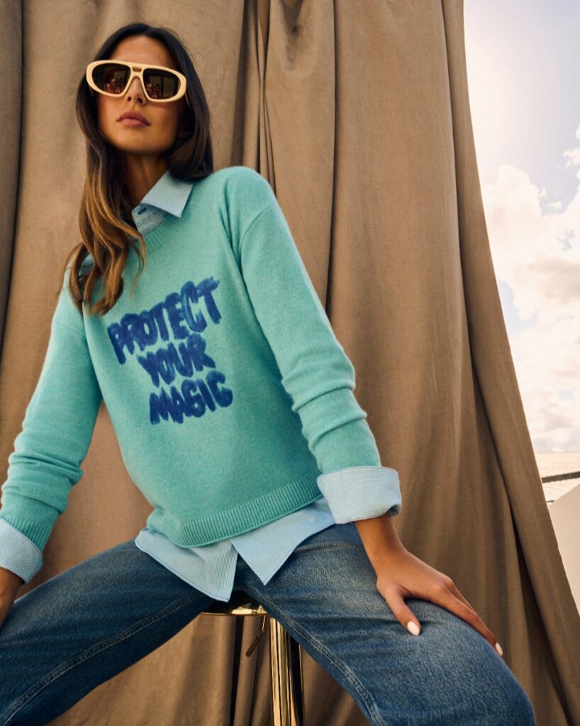 Model wearing a light blue Lisa Todd "Protect Your Magic" cashmere sweater over a collared shirt.