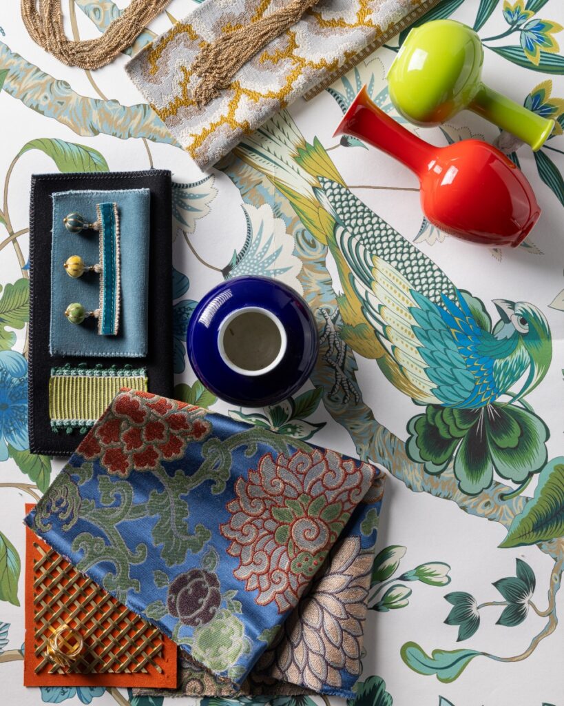 Interior design mood board with floral wallpaper, rich fabrics, trims, and colorful porcelain vases.