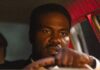 Collier’s Cuts: A Curious Moment in History Is On Display in ‘By Any Means’ A man drives a car at night with red lights glinting off the inside of the car.