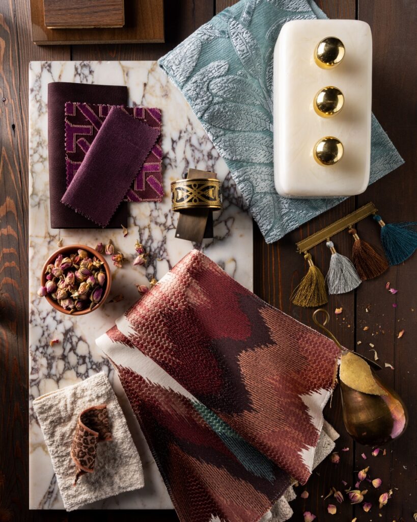 Davin Interiors jewel-toned flat lay featuring marble, rich textiles, tassel trims, and a brass pear.