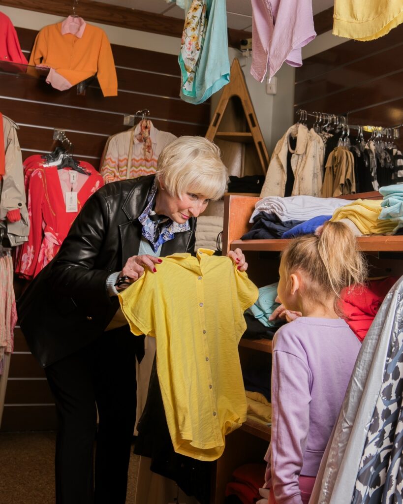 Carol Kinkela shows a yellow shirt to a young girl in her Oakmont boutique, Carabella.