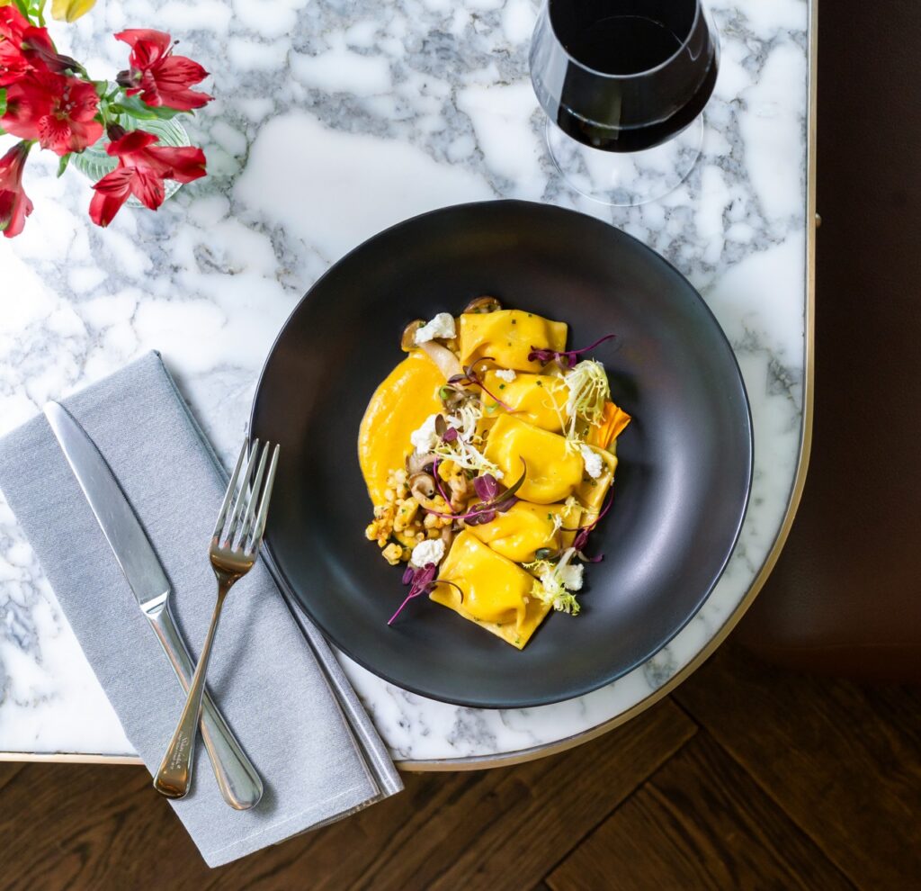 Gourmet butternut squash ravioli with mushrooms and microgreens in a black bowl.