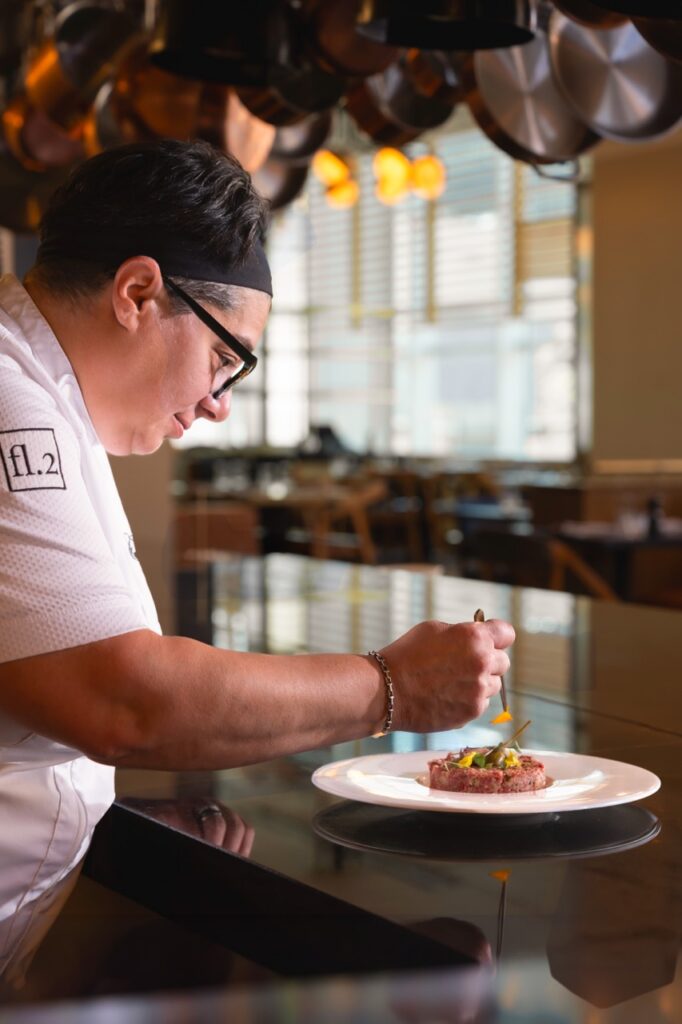 Chef plating a tartare dish with precision in a restaurant kitchen.
