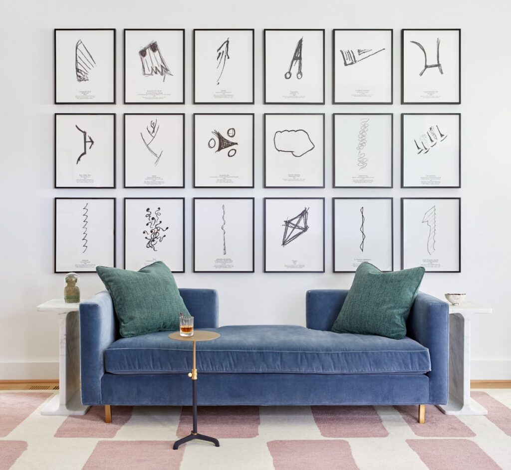 A plush blue velvet daybed accented with teal throw pillows sitting on a pink-and-white checkered rug, positioned in front of a gallery wall with an 18-frame grid of black-and-white minimalist sketches.