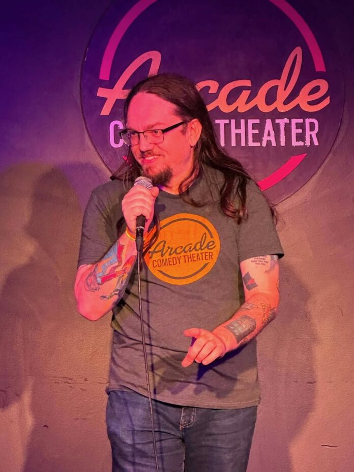 Comedian performs at Arcade Comedy Theater Pittsburgh, wearing a gray t-shirt.