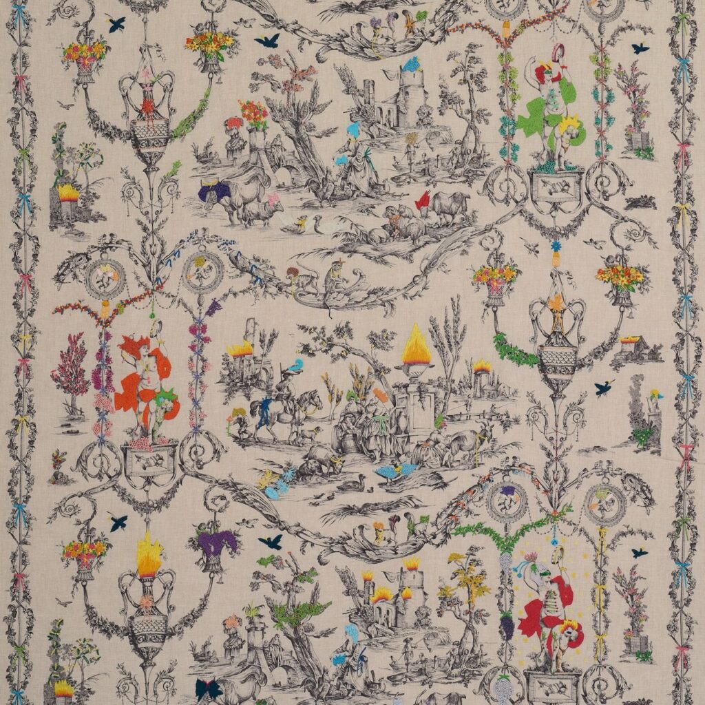 Detailed toile fabric with colorful embroidered accents, featuring pastoral scenes and ornate borders.