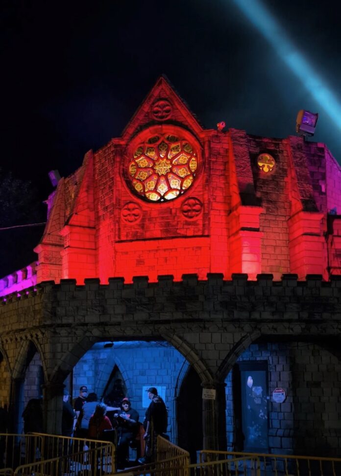 Scary Hundred Acres Manor facade at night with red and blue lights, offering tickets.