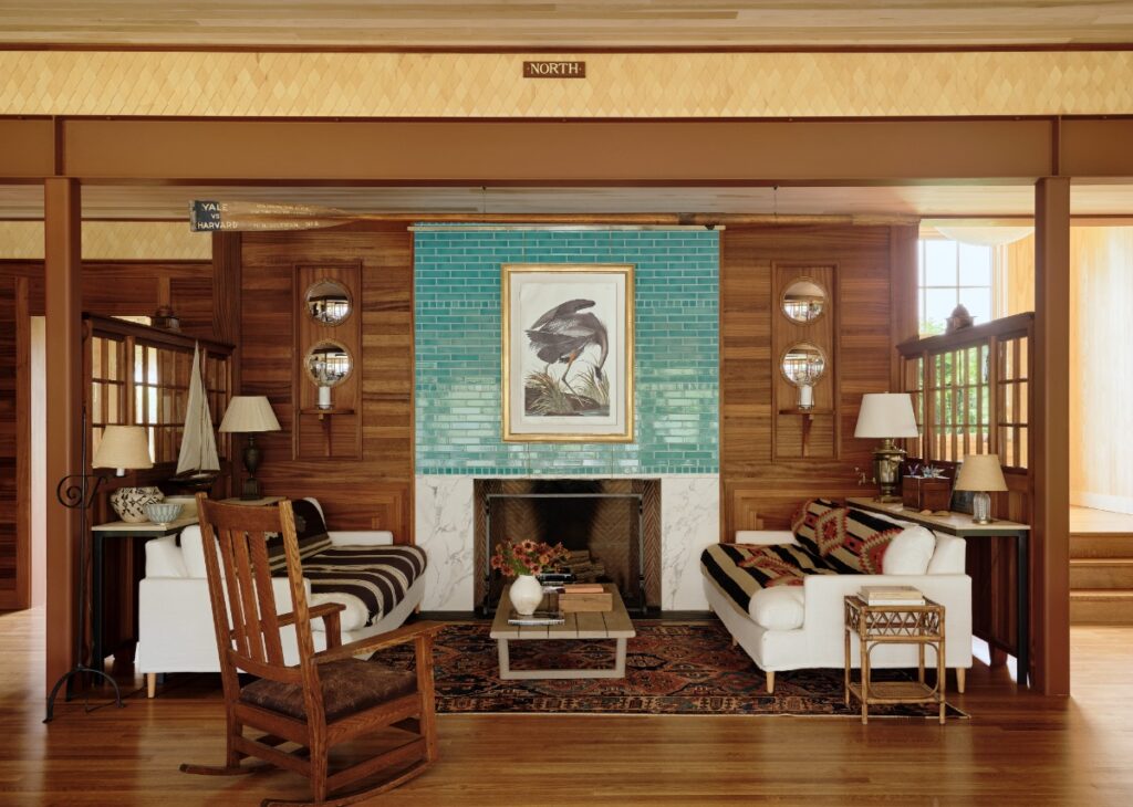 Living room snug featuring a teal tile fireplace with Audubon print, white sofas, and wood paneled walls.