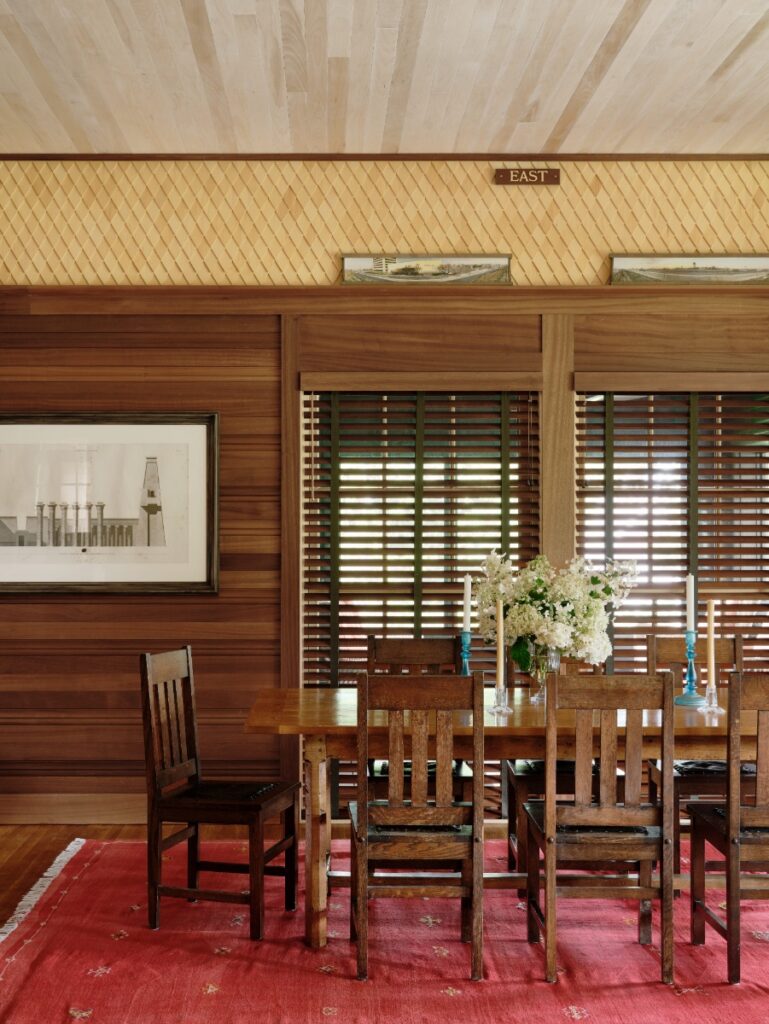 Wood-paneled dining room with wooden dining table and chairs on a red patterned rug.