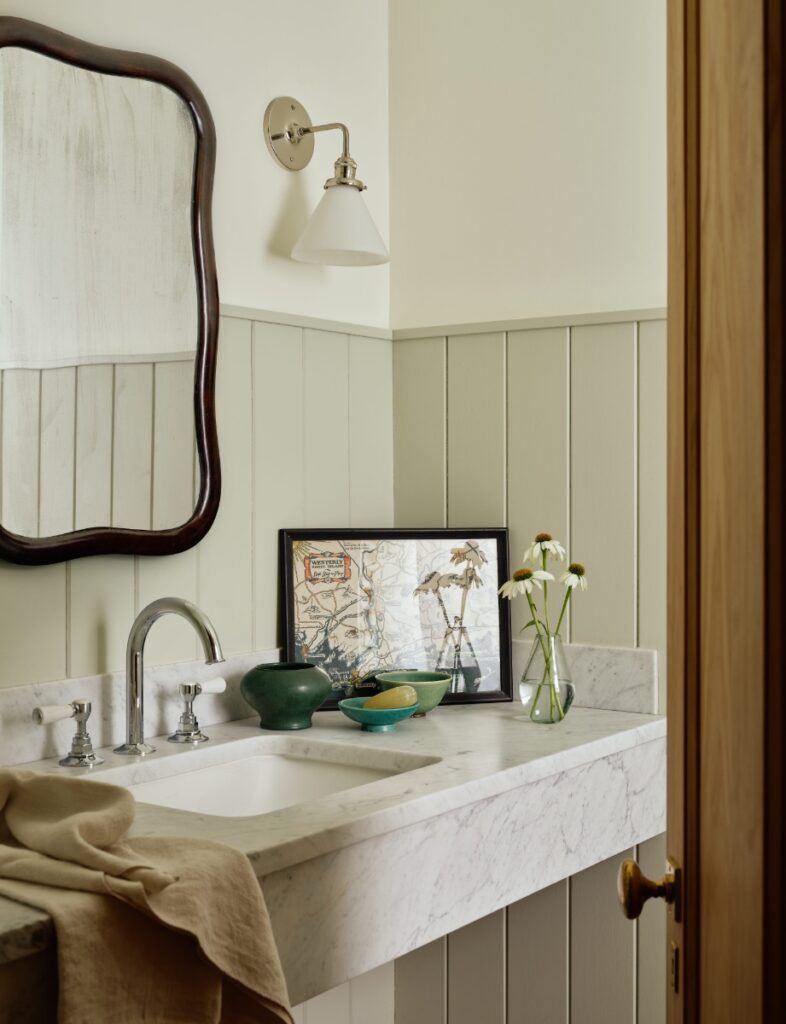 Coastal bathroom with marble vanity, wainscoting wall panels, dark wood mirror, and framed Rhode Island map.