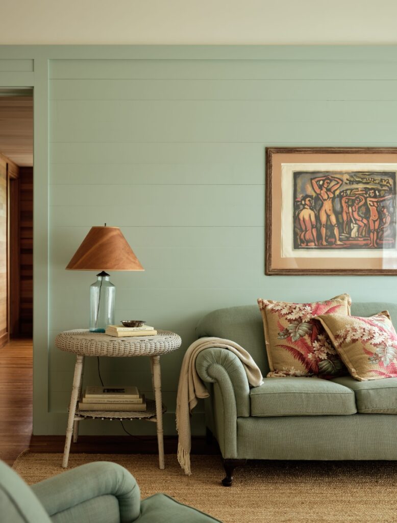 Sage green living room with a green upholstered sofa, wicker side table, and framed art.