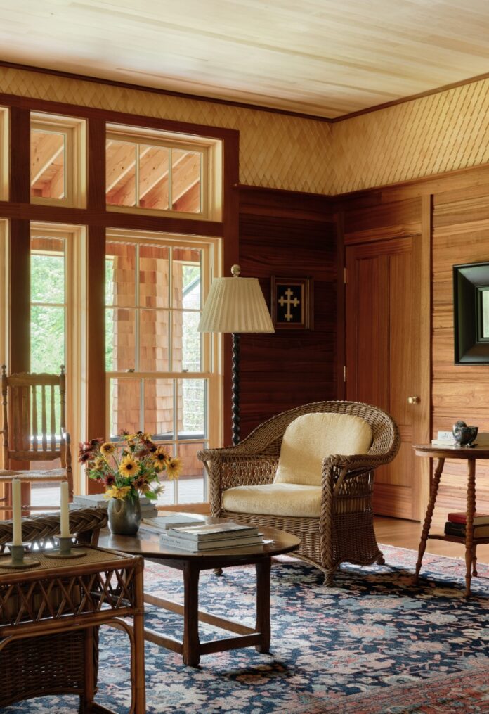 Wood-paneled living room with wicker armchair, floor lamp, large windows, and diamond wood frieze detail.