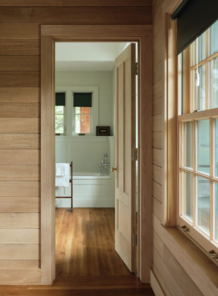Wood-paneled hallway doorway leading into a sunlit white bathroom with a soaking tub.