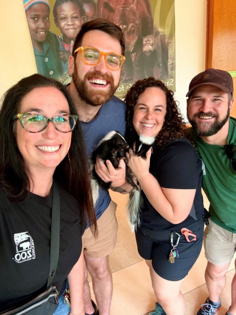 Two striped skunk sisters with four smiling people at the zoo