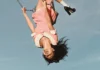 Olivia Rodrigo at PPG Paints Arena: What to Know Before You Go Olivia Rodrigo upside down on a swing, wearing a pink dress and platform heels.
