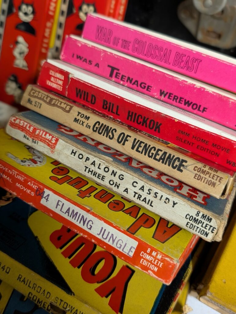 Stack of vintage movie posters and VHS tapes, including "Guns of Vengeance" and "War of the Colossal Beast.