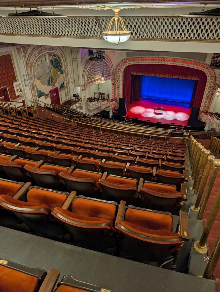 Palace Theatre auditorium with red seats and stage, offering a glimpse of the venue.