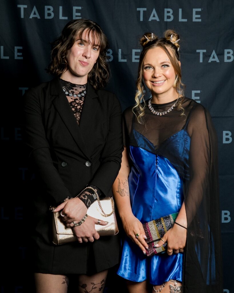 Two women in formal attire pose for a photo at an event with "TABLE" branding.