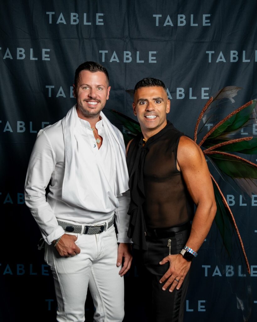 Two men posing for a photo at an event with TABLE branding and fairy wings