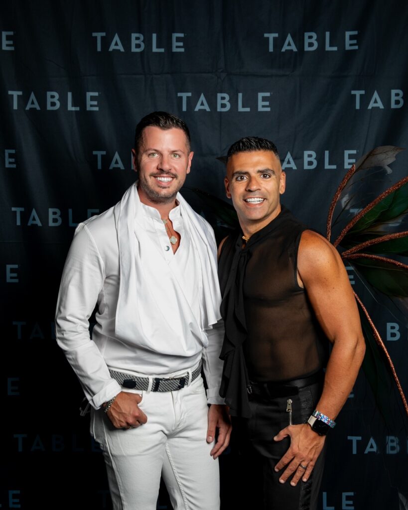 Two men in stylish outfits pose for a photo at a TABLE event