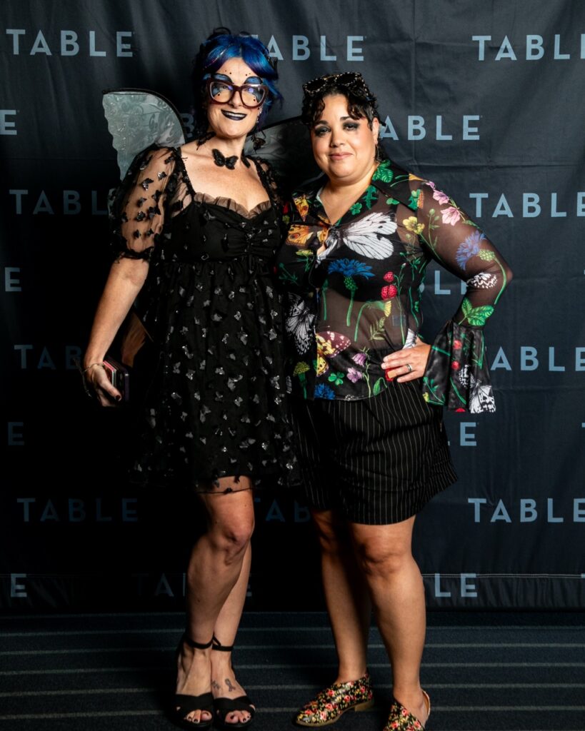 Two women in costumes pose for a photo at an event.