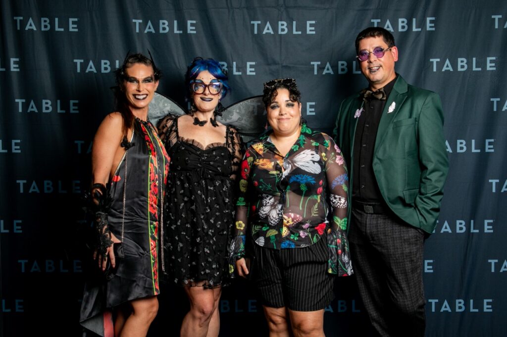 Four costumed people pose for a photo at an event with TABLE branding