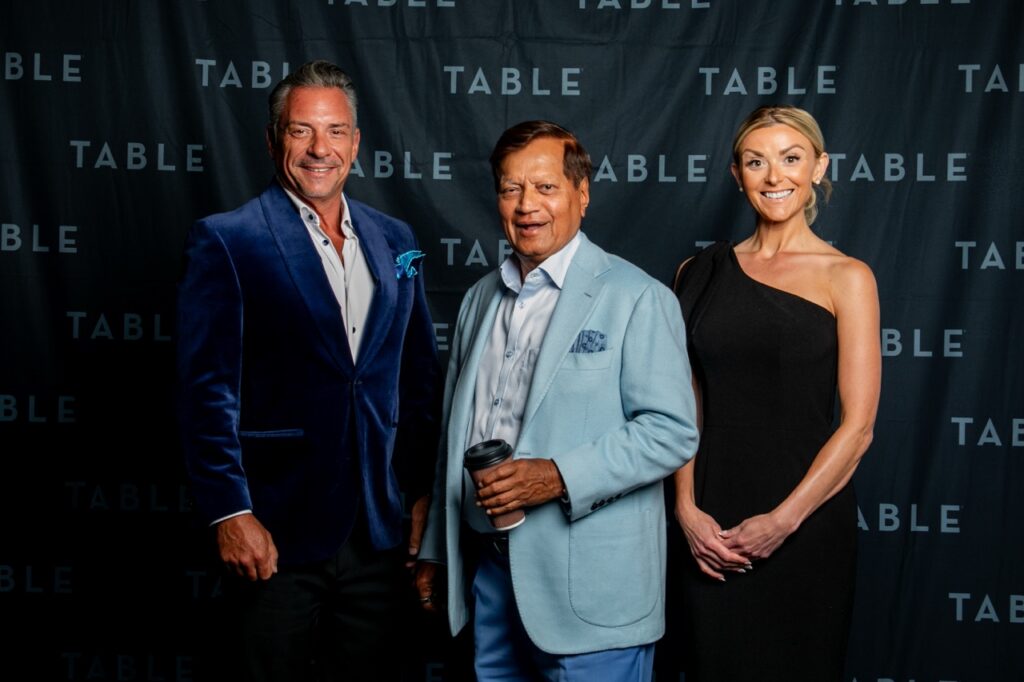 Three people pose in front of a "TABLE" backdrop.