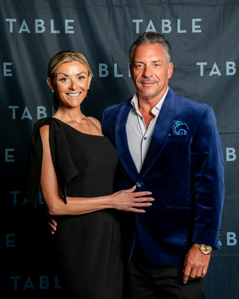 Couple posing in front of a black backdrop with "TABLE" logo