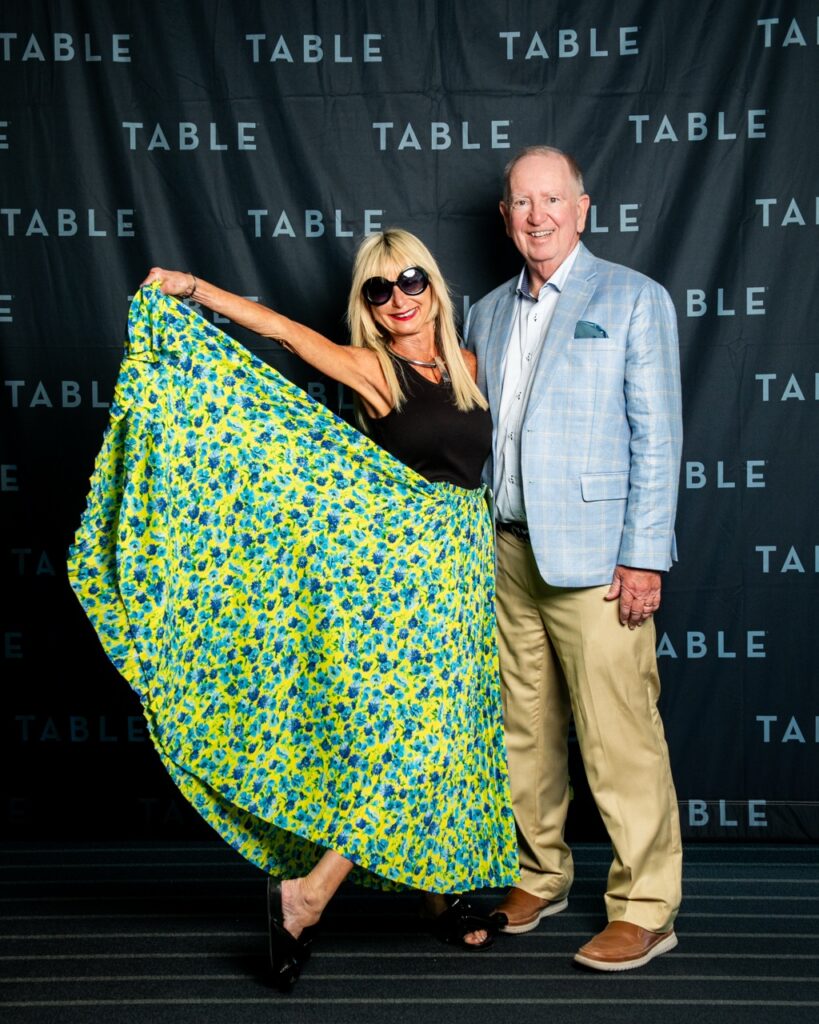 Couple poses in front of a "TABLE" backdrop at an event