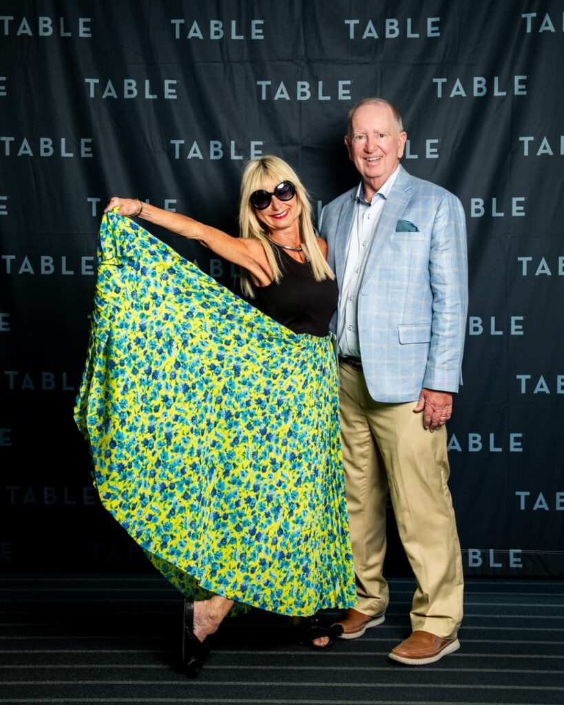 Couple posing in front of a TABLE backdrop at an event