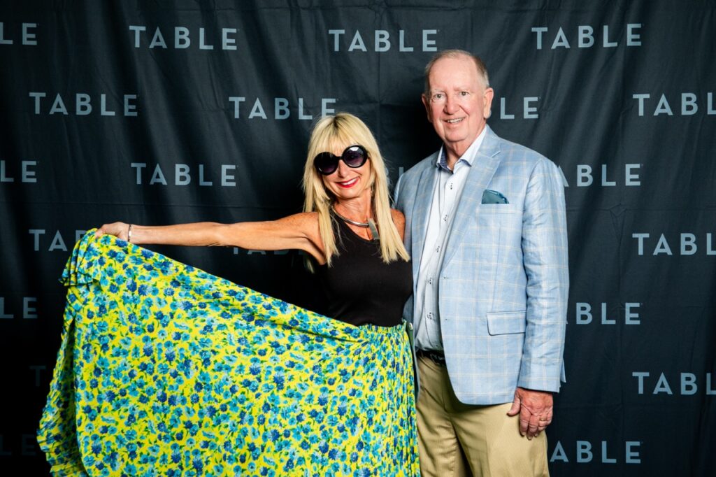 Man and woman pose in front of a "TABLE" backdrop at an event.
