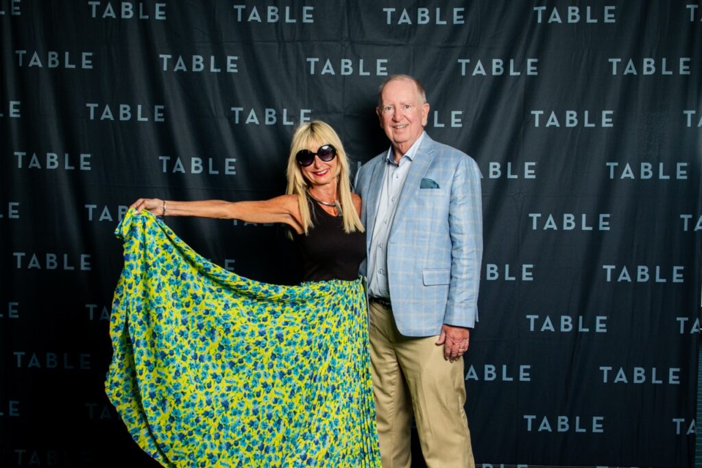 Couple poses in front of a "TABLE" backdrop at an event.
