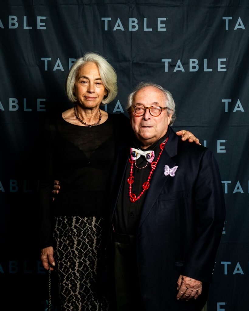 Couple posing in front of a black backdrop with "TABLE" logo.