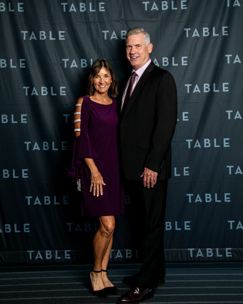 Couple posing in front of TABLE backdrop at an event.