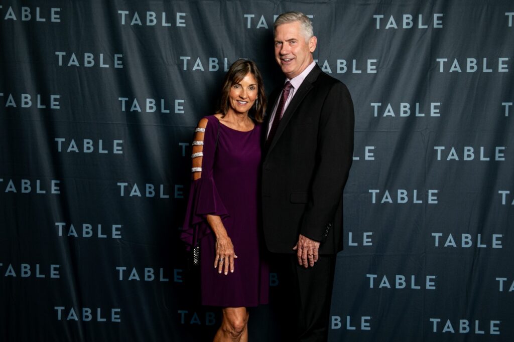 Couple posing in front of a backdrop with the word "TABLE" repeated