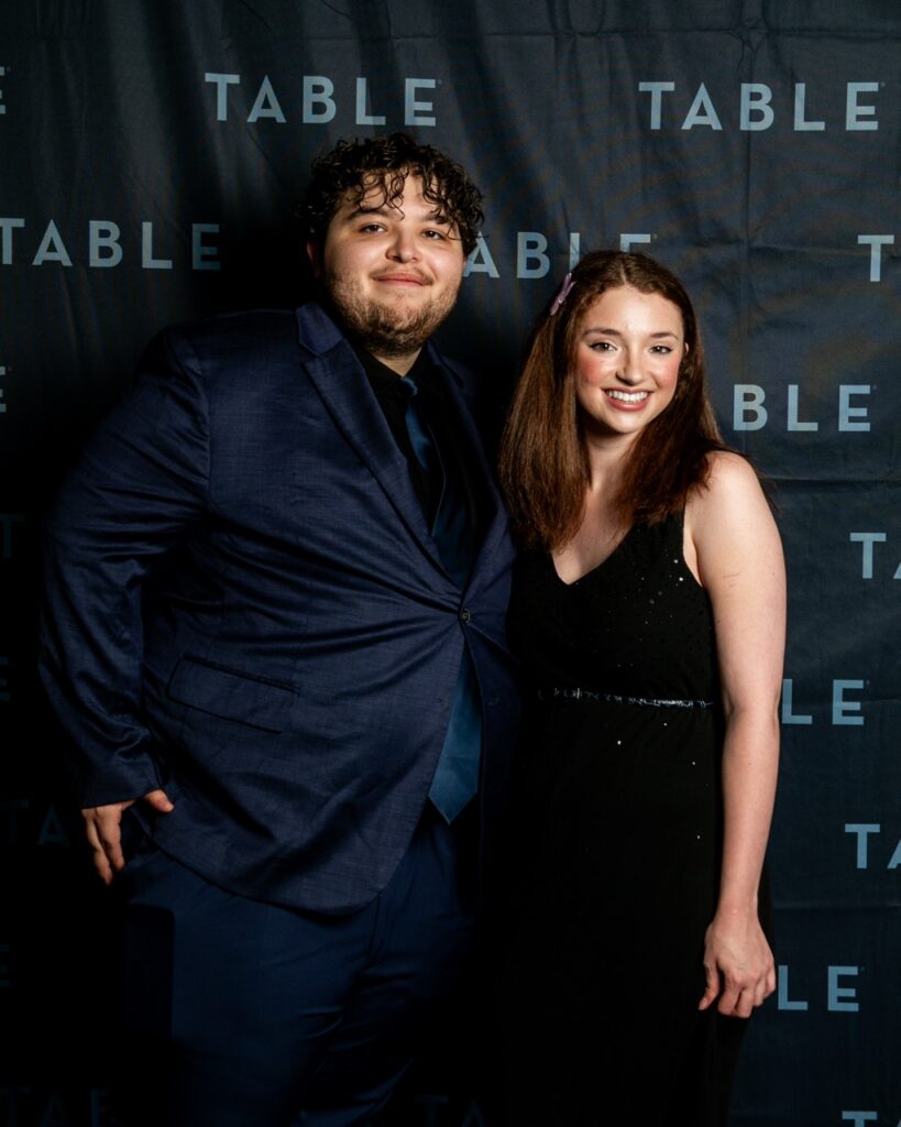 A young couple poses for a photo in front of a "TABLE" backdrop.
