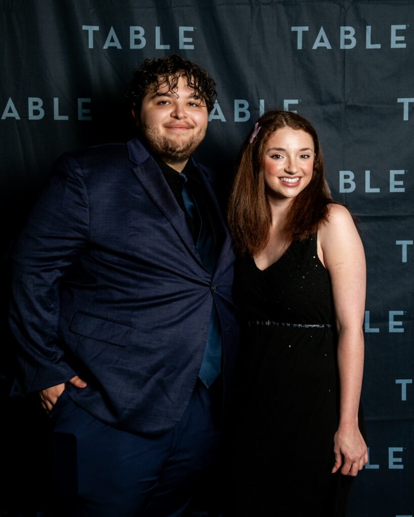Couple posing in front of a TABLE backdrop at an event.