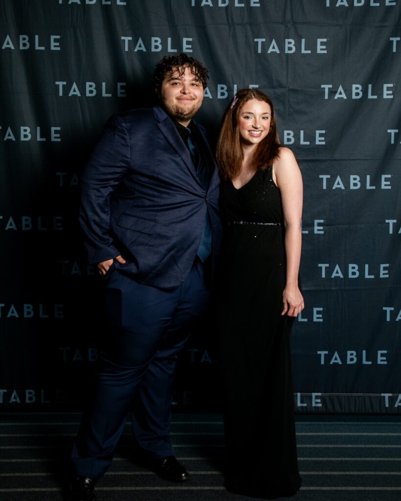 Couple posing in front of a backdrop with "TABLE" logo at an event