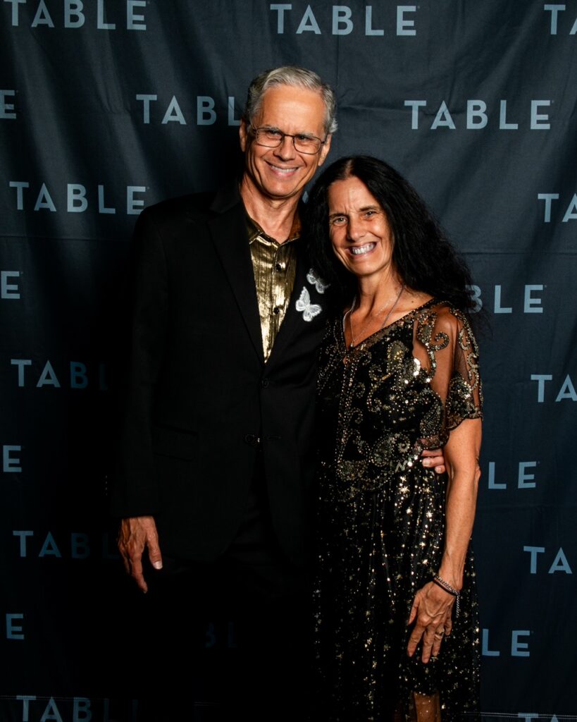 Couple in formal attire posing in front of a TABLE backdrop