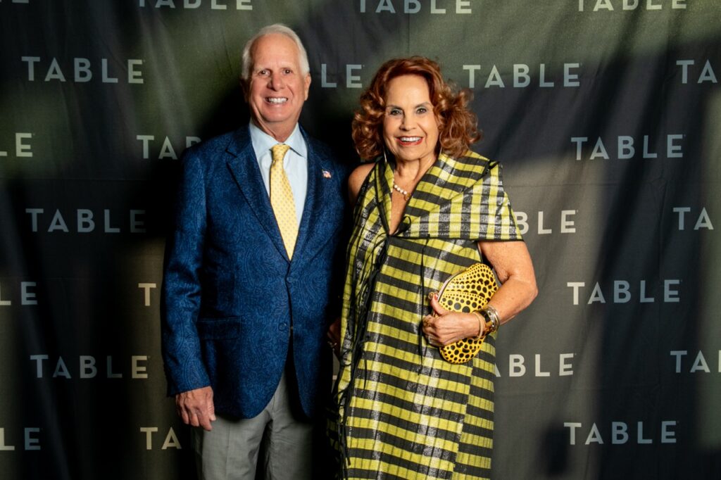 Couple in formal attire posing in front of a "TABLE" backdrop.