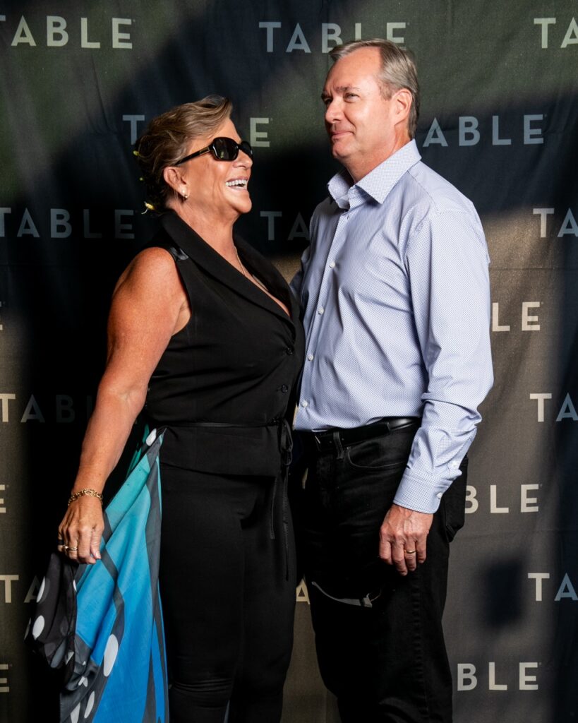 Couple smiling at each other in front of a backdrop with "TABLE" repeated